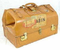 Front and side view of vintage tan leather cabin bag with leather straps, handles, brass locks, catch, and travel labels