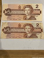 Front view of two Canadian $2 bills from 1986 showing Queen Elizabeth II portraits.