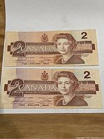 Front view of two 1986 Canadian $2 bills showing Queen Elizabeth II portrait and denomination.