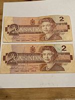 Two 1986 Canadian $2 bills laid flat showing the front side with Queen Elizabeth II portrait.