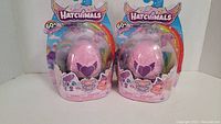 Two new Hatchimals Playdate Packs displayed side by side in their original sealed packaging. Pink eggs with purple heart design are clearly visible along with colorful branding and character artwork.