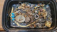 Overview of the jewelry lot showing various necklaces, pendants, and brooches in a black tray