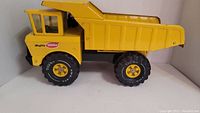 Side view of yellow Mighty Tonka metal dump truck showing dump bed, cab, and rubber tires.