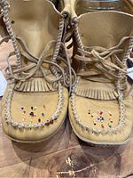 Close up image of front of leather boots showing beadwork and whipstitching.