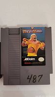 Front view of WWF WrestleMania Nintendo NES game cartridge showing label with wrestler image and Acclaim logo, with handwritten number '487'