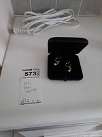 Pair of 14K gold earrings with pearl drops inside black open jewelry case on a white surface next to power cord and lot tag.