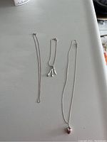 Three sterling silver jewelry items laid out: one necklace with a heart pendant, one chain necklace, and one bracelet with charms.