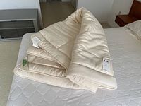 Cream-colored quilted mattress pad folded on bed, showing thick padding and quilting details.