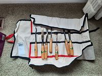 Full view of the open custom canvas case holding seven chisels, showing wooden handles and blades in individual slots.