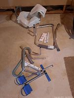 Commode with white padded seat and backrest, metal safety rails, and rowing exercise equipment with blue foot straps.
