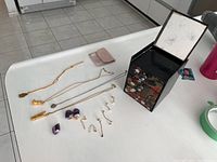 All jewelry items including necklaces, earrings, stone pendants, and jewelry box arranged on a white surface