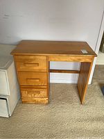 Front view of wooden desk with three drawers on left side and flat tabletop.