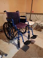 Blue and black Drive folding manual wheelchair positioned in basement with visible fabric seat, armrests, footrests, and wheels.