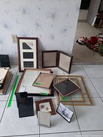 Multiple wood and metal picture frames with glass, shown grouped together on a tiled floor with a floral wallpaper background.