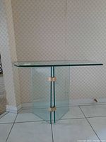 Front view of the glass hallway table showing rectangular clear glass top and metal band accents on vertical glass panels.