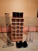 Front view of wood CD rack with multiple slots, wooden CD holder with compartments placed on top, metal wire CD holder to the right, black triangular CD holders in front, set against a bare wall and exposed insulation behind.