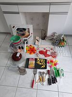 Full assortment of kitchen accessories arranged on floor showing knives, corn holders, salt and pepper shakers, placemats, napkin rings, hangers, bowls, pitcher, and plastic green ice cream cups.