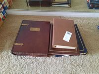 Four photo albums and a large wooden memory box stacked on beige carpet near mirror