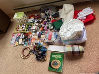 Full overview of lot showing multiple sewing and craft supplies laid out on carpet including thread, fabric, pins, buttons, embroidery hoops, and book