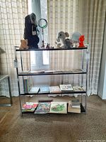 Front view of the metal shelf unit against a window, showing four shelves with various items on top and on shelves.