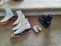 Photo of two pairs of white women's ice skates (sizes 5 and 7), small white baby shoes, and a black and grey scuba diving shoe.