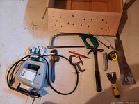 Photo showing the full set of hand tools including Sabre saw, hammer, pipe wrench, tape measure, and other tools lying on floor next to cardboard box.