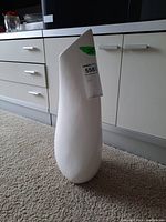 White ceramic vase with teardrop shape and slanted top opening, placed on carpet in kitchen environment