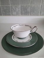 Teacup, saucer, and flat side plate arranged on countertop with tiled background