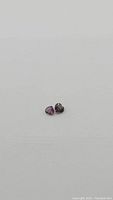 Photo showing two small heart-shaped sapphires on a white background, highlighting size and color difference.