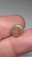 Close-up photo of the cushion cabochon Ethiopian opal gemstone held between fingers showing color play and translucency.