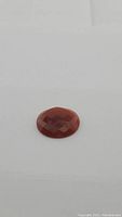 Close-up photo of the deep orange oval carnelian gemstone showing the checkerboard faceted cabochon cut and polished surface.