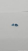 Photo of two pear cut London blue topaz gemstones lying flat on white background showing deep blue color and facets.
