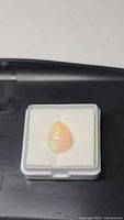 Untreated Ethiopian opal pear cabochon gemstone inside a clear display box on white foam.