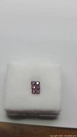 Five deep blood red, purple-tone octagon cut rubies arranged on white display, approximately 3x3mm each.