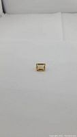 Natural golden citrine gemstone, emerald cut, placed on white background, showing rectangular shape and facets.