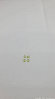 Four natural apple green peridot gemstones about 5mm each placed on a white background for size and color display.