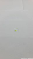 Top-down view of a small oval apple green peridot gemstone on white background highlighting color and cut.