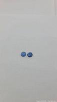 Two round blue kyanite cabochon gemstones on white background, showing size and color.