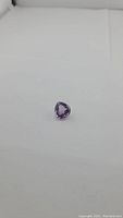 Photo showing a natural pear cut purple amethyst gemstone on a white surface, highlighting color and cut.