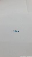 Four small bright Swiss blue topaz gemstones laid flat on a white background, showing their calibrated size and shape.
