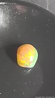 Top-down close-up of cushion cabochon natural chocolate opal resting in a black dish showing bright rainbow flash and glowing red fiery colors.