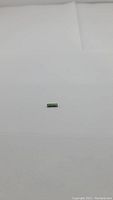 Rectangular cut natural green tourmaline gemstone on plain white background, showing size and color.
