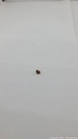 Photo of a small natural deep orange champagne colored heart-shaped zircon gemstone on white background, showing clear facets and color.