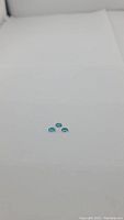 Three small, oval-shaped, bright blue gemstones on a white background, showing size and color.