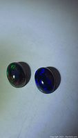Two jet black opals on white background showing multicolored flashes including green, red, and blue.