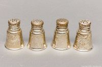Four sterling silver salt and pepper shakers arranged side by side showing front and side views, minor tarnishing visible