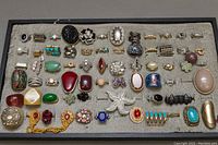View of entire assortment of costume rings laid on fabric covered tray, showing variety of colors, shapes, and materials.