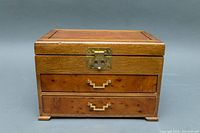 Closed wooden jewelry box with brass handle and latch shown from front.