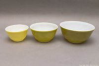 Three Pyrex mixing bowls in descending size order, showing front and all three colors: yellow and olive green with white interiors.