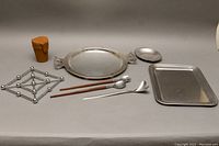 Photo showing all items including WMF round tray, salad tongs, Cross cup set in leather case, rectangular tray, small dish, metal trivet and bent utensil